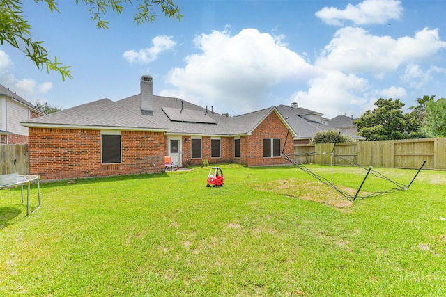 18115 Stone Angel Dr, Humble, TX 77346 - rear view of property featuring a trampoline, a fenced backyard, roof mounted solar panels, brick siding, and a chimney