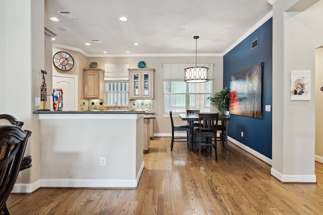 5706 Blossom St, Houston, TX 77007 - kitchen with ornamental molding, dark countertops, glass insert cabinets, light wood finished floors, and pendant lighting