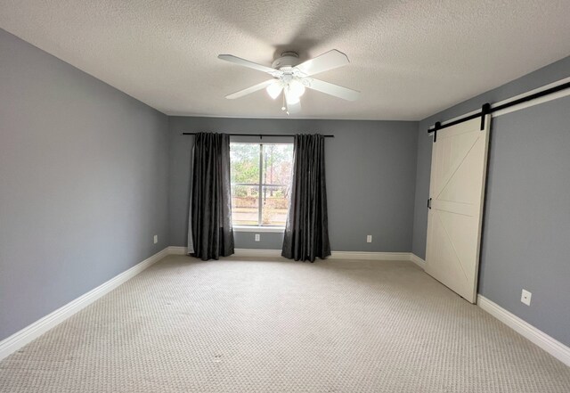 1023 Fountain View Dr, Houston, TX 77057 - unfurnished bedroom featuring light carpet, a textured ceiling, a barn door, and ceiling fan