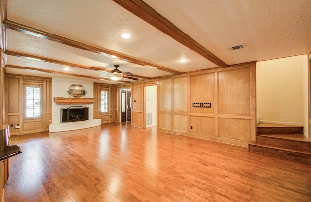 3623 Beech Hill Dr, Spring, TX 77388 - unfurnished living room with a textured ceiling, light wood finished floors, beamed ceiling, a fireplace with raised hearth, and a decorative wall