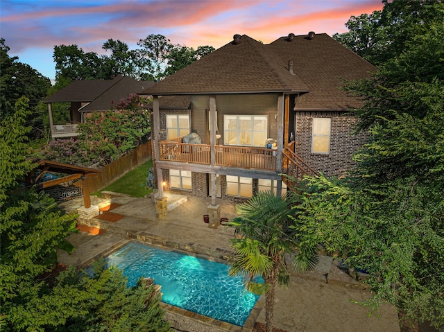 1207 Marigold Ln, Longview, TX 75604 - back of property at dusk featuring a shingled roof, a patio area, a balcony, and an outdoor pool