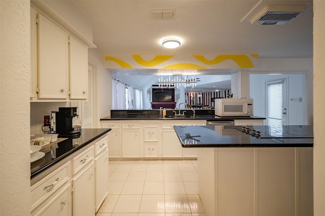 10730 Braes Bayou Dr, Houston, TX 77071 - kitchen featuring white microwave, a peninsula, dark countertops, light tile patterned floors, and white cabinetry