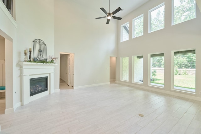 237 Patina Sorrel Dr, Montgomery, TX 77316 - unfurnished living room with a towering ceiling, a glass covered fireplace, a ceiling fan, and light wood finished floors