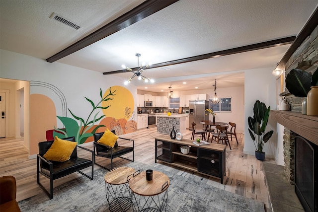 5918 Lattimer Dr, Houston, TX 77035 - living area with a chandelier, light wood-type flooring, beamed ceiling, a textured ceiling, and a fireplace with raised hearth
