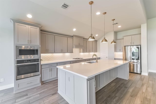 20519 Grazing Foal Ln, Tomball, TX 77377 - kitchen with stainless steel appliances, gray cabinetry, light wood-style flooring, a kitchen island with sink, and backsplash