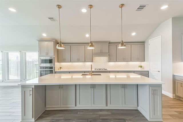 20519 Grazing Foal Ln, Tomball, TX 77377 - kitchen with appliances with stainless steel finishes, gray cabinetry, backsplash, an island with sink, and wood finished floors