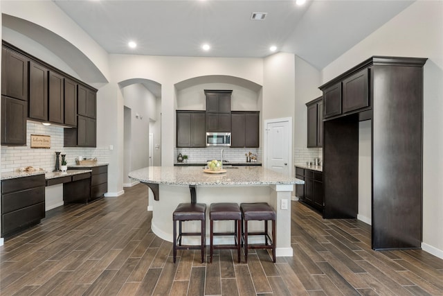16711 Ramsay Cascades Dr, Humble, TX 77346 - kitchen with stainless steel microwave, a center island, dark brown cabinetry, backsplash, and recessed lighting