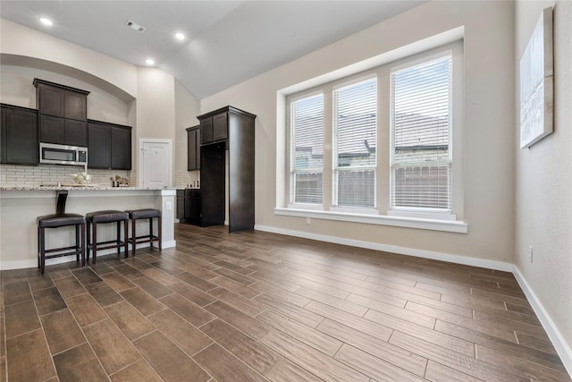 16711 Ramsay Cascades Dr, Humble, TX 77346 - kitchen featuring stainless steel microwave, a breakfast bar, decorative backsplash, lofted ceiling, and dark wood-style flooring