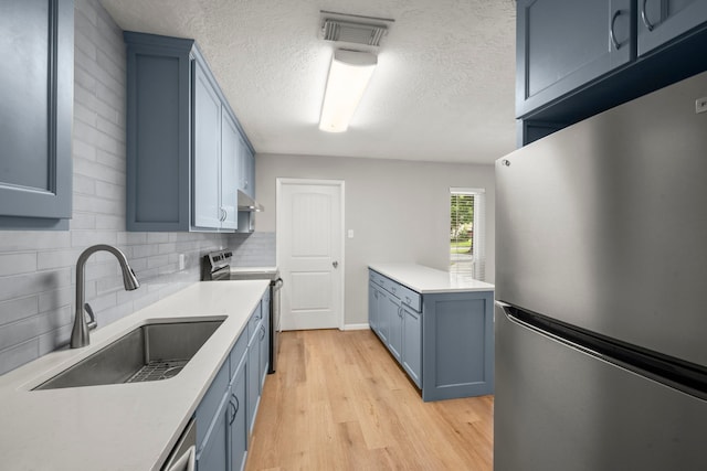 14902 Forest Lodge Dr, Houston, TX 77070 - kitchen with appliances with stainless steel finishes, blue cabinetry, a textured ceiling, light countertops, and backsplash
