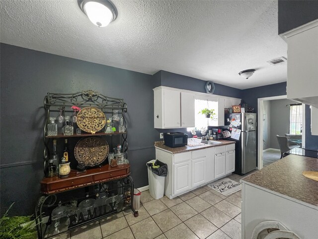 3412 Lantern Ln, Baytown, TX 77521 - kitchen with freestanding refrigerator, a textured ceiling, light tile patterned flooring, white cabinets, and dark countertops