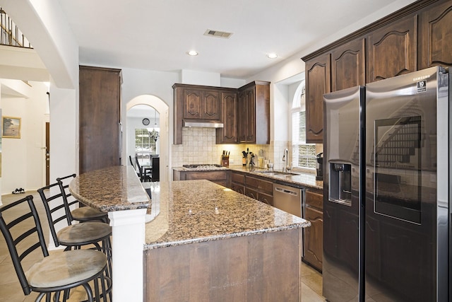 20692 Oakhurst Meadows Dr, Porter, TX 77365 - kitchen featuring stainless steel appliances, a breakfast bar area, backsplash, arched walkways, and stone counters