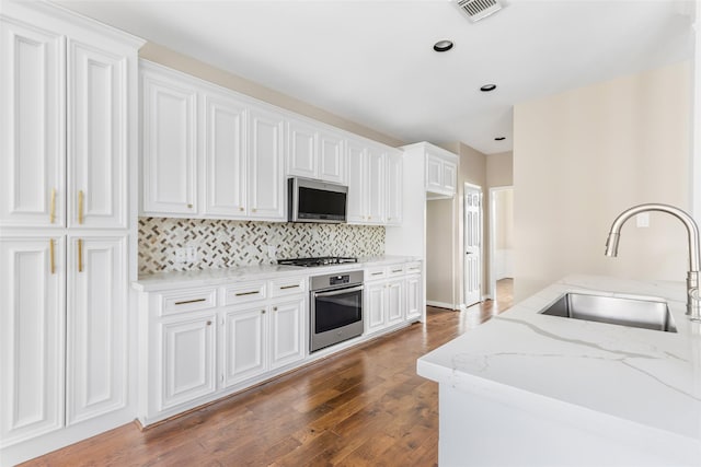 7127 Vermejo Park Ln, Humble, TX 77346 - kitchen with appliances with stainless steel finishes, light stone countertops, tasteful backsplash, dark wood-type flooring, and white cabinetry