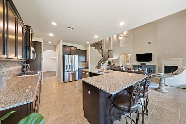 10002 Mahaffey Rd, Tomball, TX 77375 - kitchen featuring stainless steel appliances, arched walkways, a spacious island, dark brown cabinets, and a glass covered fireplace