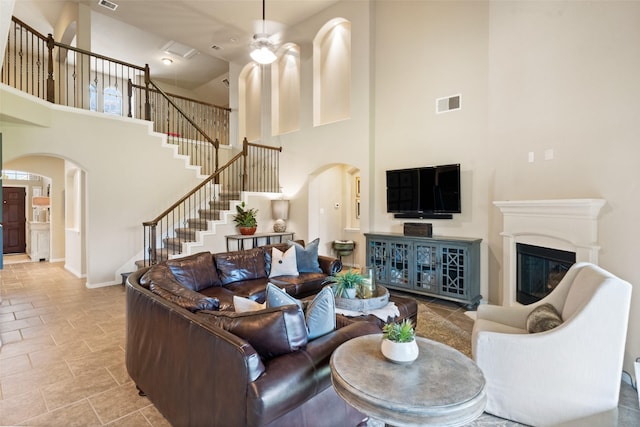 10002 Mahaffey Rd, Tomball, TX 77375 - living room featuring arched walkways, a towering ceiling, stairs, a glass covered fireplace, and a ceiling fan