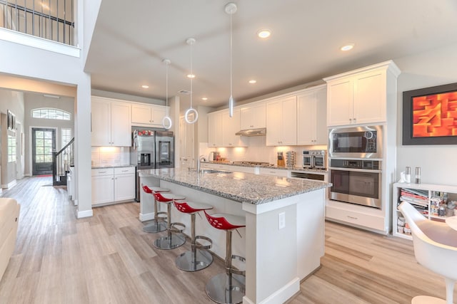 40 Snowdrop Lily Dr, Tomball, TX 77375 - kitchen featuring appliances with stainless steel finishes, light wood-style flooring, decorative backsplash, a kitchen island with sink, and a breakfast bar area