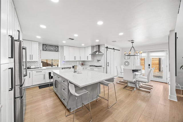 5122 Glenmeadow Dr, Houston, TX 77096 - kitchen with wall chimney range hood, a barn door, decorative backsplash, white cabinetry, and light wood finished floors