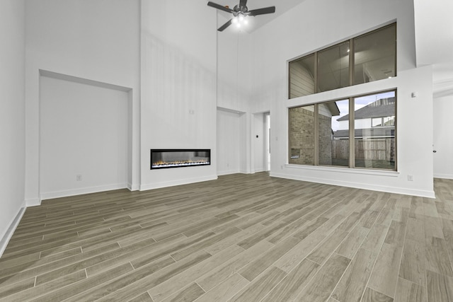 1168 Beals Creek St, Conroe, TX 77304 - unfurnished living room with a high ceiling, wood finished floors, a glass covered fireplace, and a ceiling fan