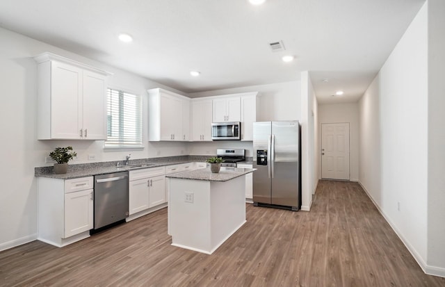 25565 Balsamroot Dr, Magnolia, TX 77355 - kitchen featuring appliances with stainless steel finishes, wood finished floors, white cabinets, a kitchen island, and recessed lighting