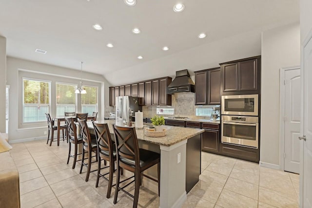 166 Hearthshire Cir, Magnolia, TX 77354 - kitchen with stainless steel appliances, wall chimney exhaust hood, an island with sink, dark brown cabinets, and a breakfast bar