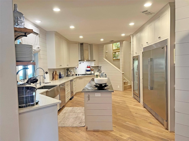 1234 Challenger, Lakeway, TX 78734 - kitchen featuring stainless steel appliances, wall chimney range hood, a kitchen island, light wood-style floors, and white cabinetry