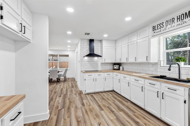 17207 Hill View Ln, Spring, TX 77379 - kitchen featuring butcher block countertops, wall chimney range hood, backsplash, light wood finished floors, and white cabinets