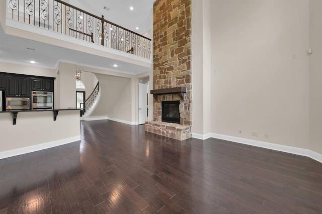 3403 Wooded Ln, Conroe, TX 77301 - unfurnished living room with a towering ceiling, stairway, dark wood finished floors, a stone fireplace, and recessed lighting