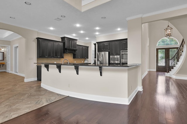 3403 Wooded Ln, Conroe, TX 77301 - kitchen featuring appliances with stainless steel finishes, a breakfast bar, arched walkways, dark cabinetry, and ornamental molding