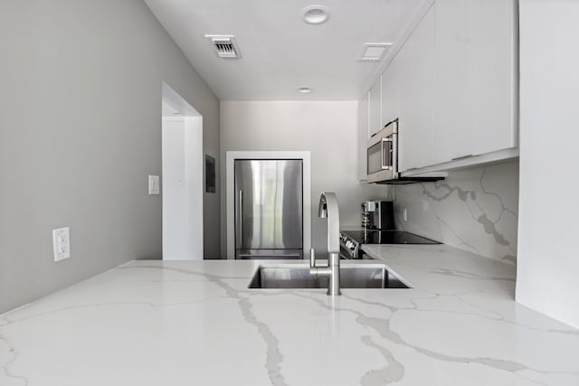 3600 Montrose Blvd Unit 209, Houston, TX 77006 - kitchen featuring appliances with stainless steel finishes, white cabinets, light stone counters, and backsplash