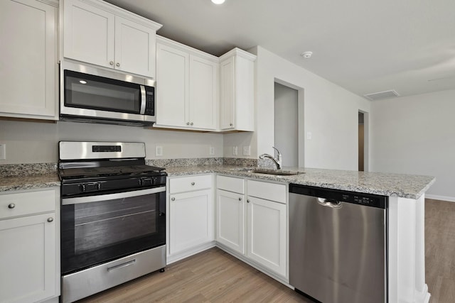 396 Tejas Trl, Waller, TX 77484 - kitchen featuring appliances with stainless steel finishes, light wood finished floors, a peninsula, and white cabinets