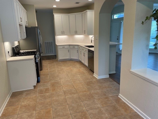 2111 Ridge Wood Ln, Sugar Land, TX 77479 - kitchen featuring appliances with stainless steel finishes, arched walkways, tasteful backsplash, white cabinetry, and light countertops