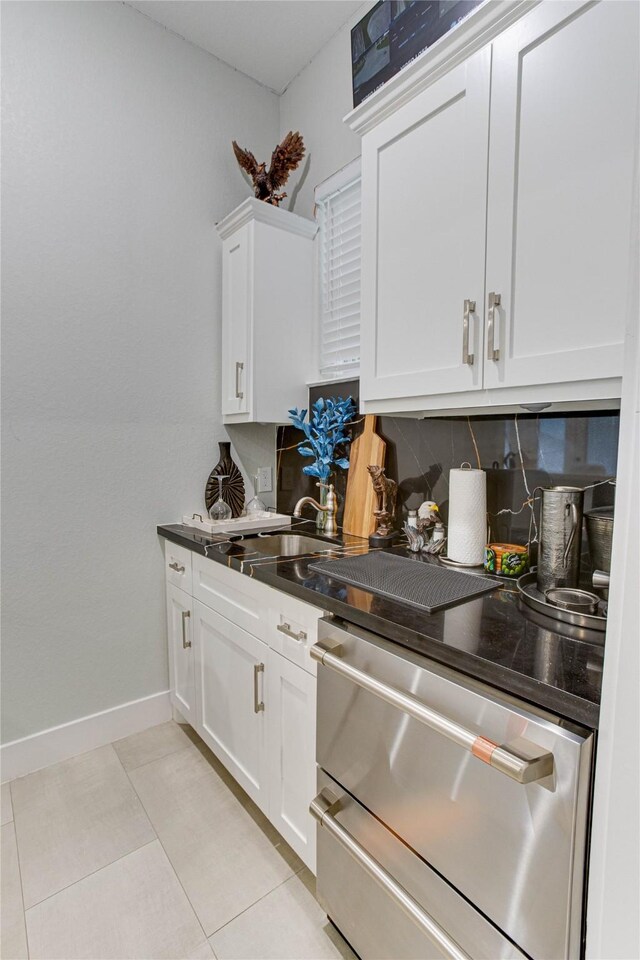 4821 1st St, Houston, TX 77504 - kitchen featuring stainless steel dishwasher, tasteful backsplash, white cabinets, light tile patterned floors, and dark countertops