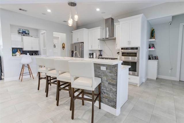 4821 1st St, Houston, TX 77504 - kitchen featuring wall chimney exhaust hood, stainless steel appliances, a breakfast bar area, white cabinets, and hanging light fixtures