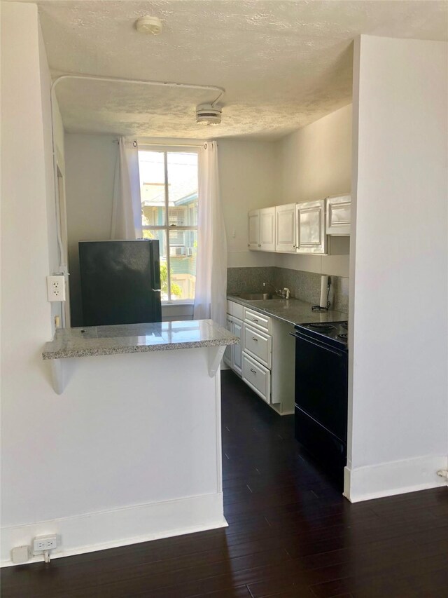 915 11th St, Galveston, TX 77550 - kitchen featuring black appliances, dark wood-style floors, white cabinetry, a textured ceiling, and light stone counters