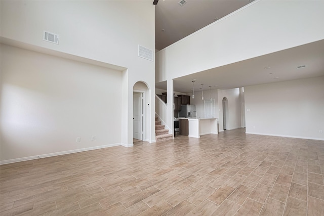 10023 Rose Mallow Ln, Magnolia, TX 77354 - unfurnished living room with arched walkways, light wood-type flooring, a towering ceiling, stairway, and ceiling fan