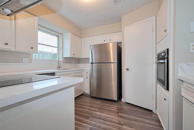 4307 Jura Dr, Houston, TX 77084 - kitchen featuring appliances with stainless steel finishes, dark wood-type flooring, light countertops, white cabinetry, and a textured ceiling