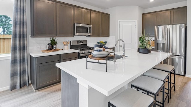 1219 Buffalo Run, Tomball, TX 77375 - kitchen featuring stainless steel appliances, dark brown cabinets, a breakfast bar area, decorative backsplash, and light wood-style floors