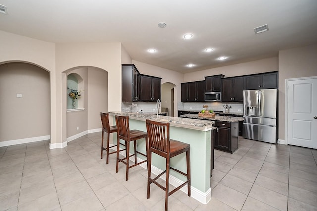 20202 Sienna Bluff Dr, Cypress, TX 77433 - kitchen featuring stainless steel appliances, arched walkways, decorative backsplash, a kitchen bar, and recessed lighting