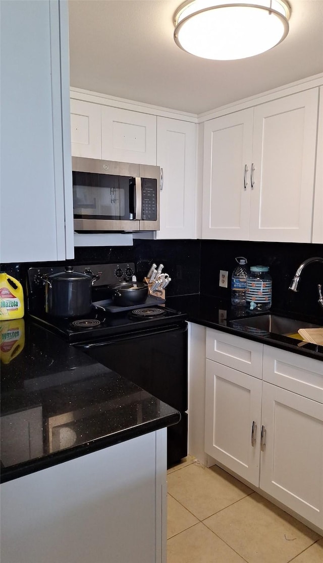 7510 Hornwood, Houston, TX 77036 - kitchen with stainless steel microwave, electric range, light tile patterned floors, white cabinets, and decorative backsplash