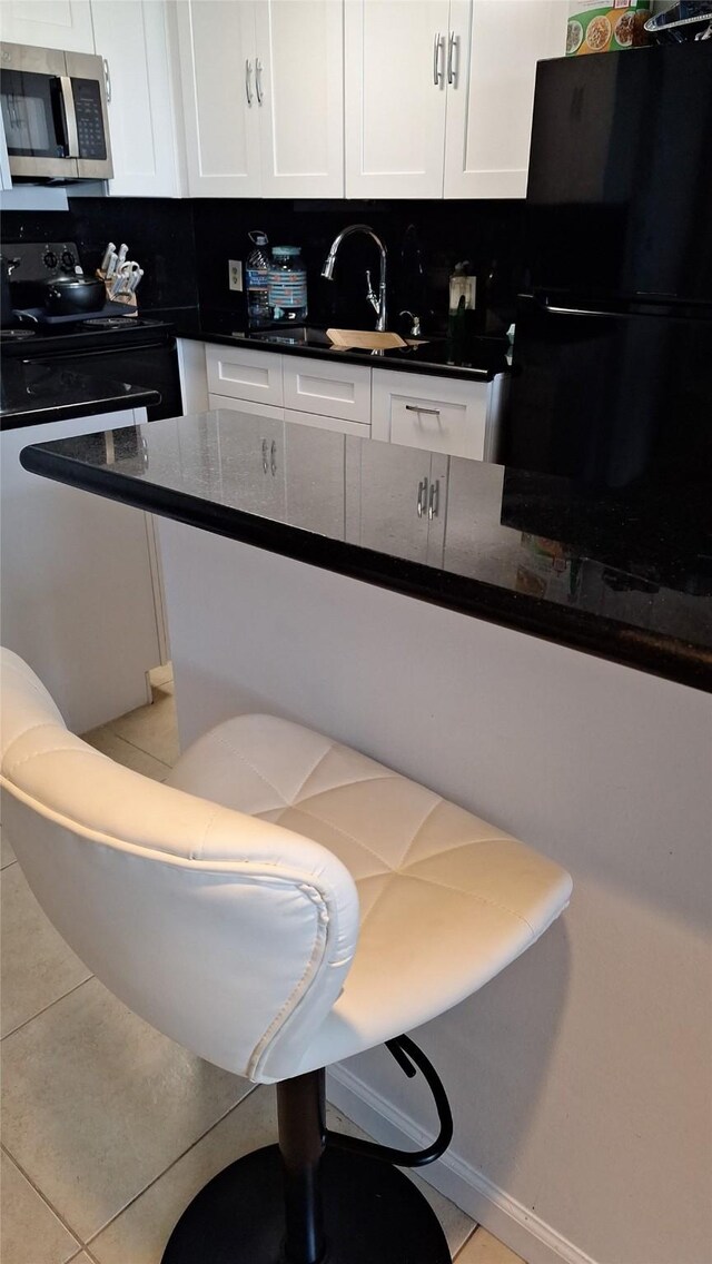 7510 Hornwood, Houston, TX 77036 - kitchen with stainless steel microwave, freestanding refrigerator, white cabinets, tile patterned floors, and dark stone counters
