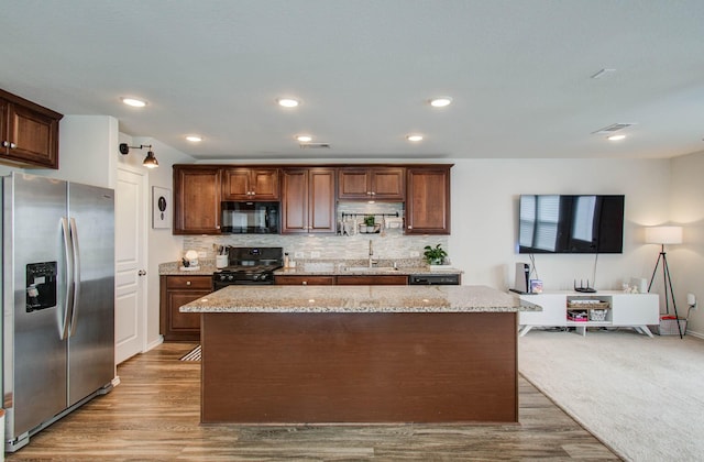 14746 Jasper Stream Ct, Houston, TX 77069 - kitchen featuring black appliances, a kitchen island, wood finished floors, light stone counters, and backsplash