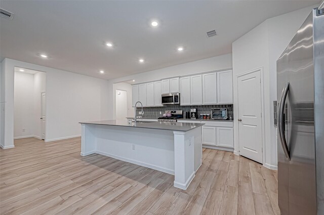 23722 Canolo Grove Ln, New Caney, TX 77357 - kitchen featuring stainless steel appliances, tasteful backsplash, light wood-style flooring, an island with sink, and white cabinets