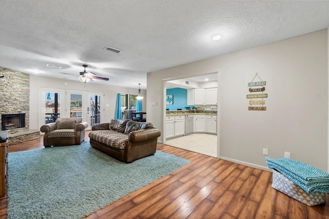 145 Capetown, Montgomery, TX 77356 - living room featuring light wood-style floors, a textured ceiling, ceiling fan, and a stone fireplace