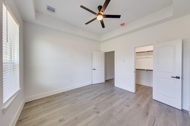 25050 Shady Oak Dr, Hockley, TX 77447 - unfurnished bedroom with a tray ceiling, multiple windows, light wood finished floors, and a walk in closet