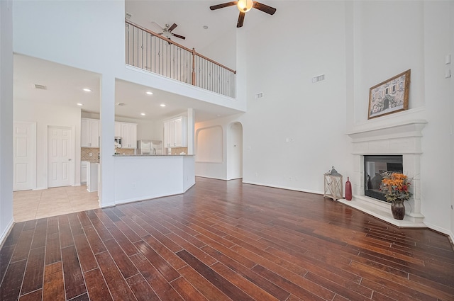 4142 Regal Stone Ln, Sugar Land, TX 77479 - unfurnished living room with a ceiling fan, a towering ceiling, wood finished floors, a glass covered fireplace, and arched walkways