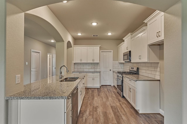 10477 Valley Dr N, Willis, TX 77318 - kitchen with appliances with stainless steel finishes, arched walkways, white cabinetry, wood finished floors, and recessed lighting