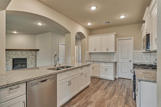 10477 Valley Dr N, Willis, TX 77318 - kitchen featuring appliances with stainless steel finishes, white cabinetry, arched walkways, wood finished floors, and backsplash