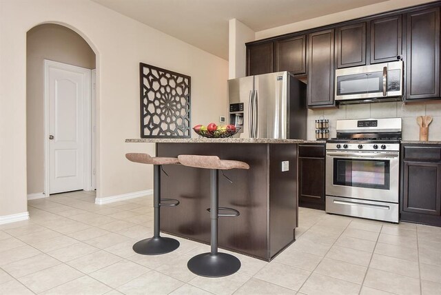 3514 Marquesa Ln, Houston, TX 77084 - kitchen with stainless steel appliances, a breakfast bar, arched walkways, and light tile patterned floors