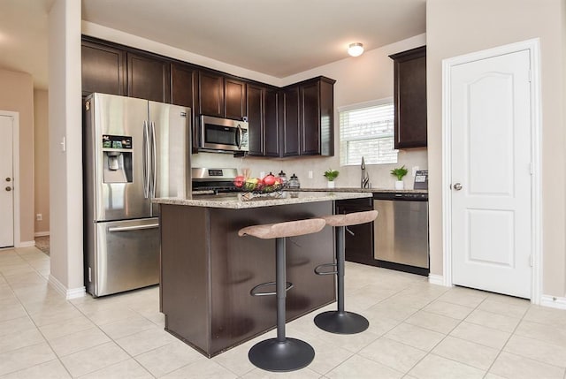 3514 Marquesa Ln, Houston, TX 77084 - kitchen featuring appliances with stainless steel finishes, a kitchen breakfast bar, dark brown cabinets, a kitchen island, and light stone countertops