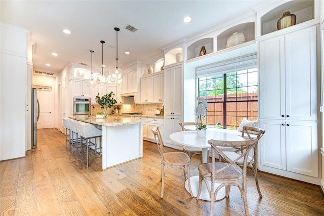 1403 Wakefield Dr, Houston, TX 77018 - kitchen with stainless steel appliances, white cabinets, a kitchen island with sink, light wood-type flooring, and a kitchen breakfast bar