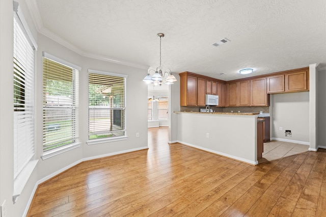 14607 Dawn Mist Ct, Magnolia, TX 77354 - kitchen featuring white microwave, a chandelier, brown cabinetry, light wood-style floors, and ornamental molding